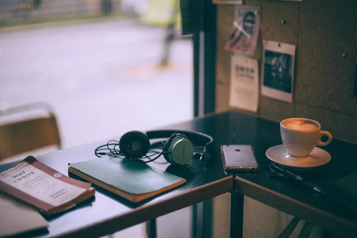 Headphones, a book, and a cappuccino on a cafe table — everyday background music shapes our experience without us noticing